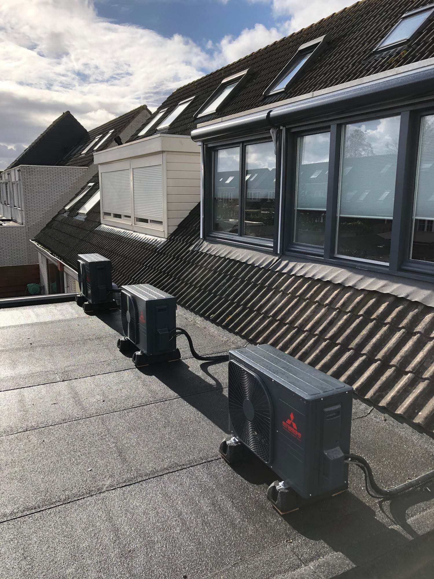 Drie airco-buitenunits op een plat dak naast dakkapellen