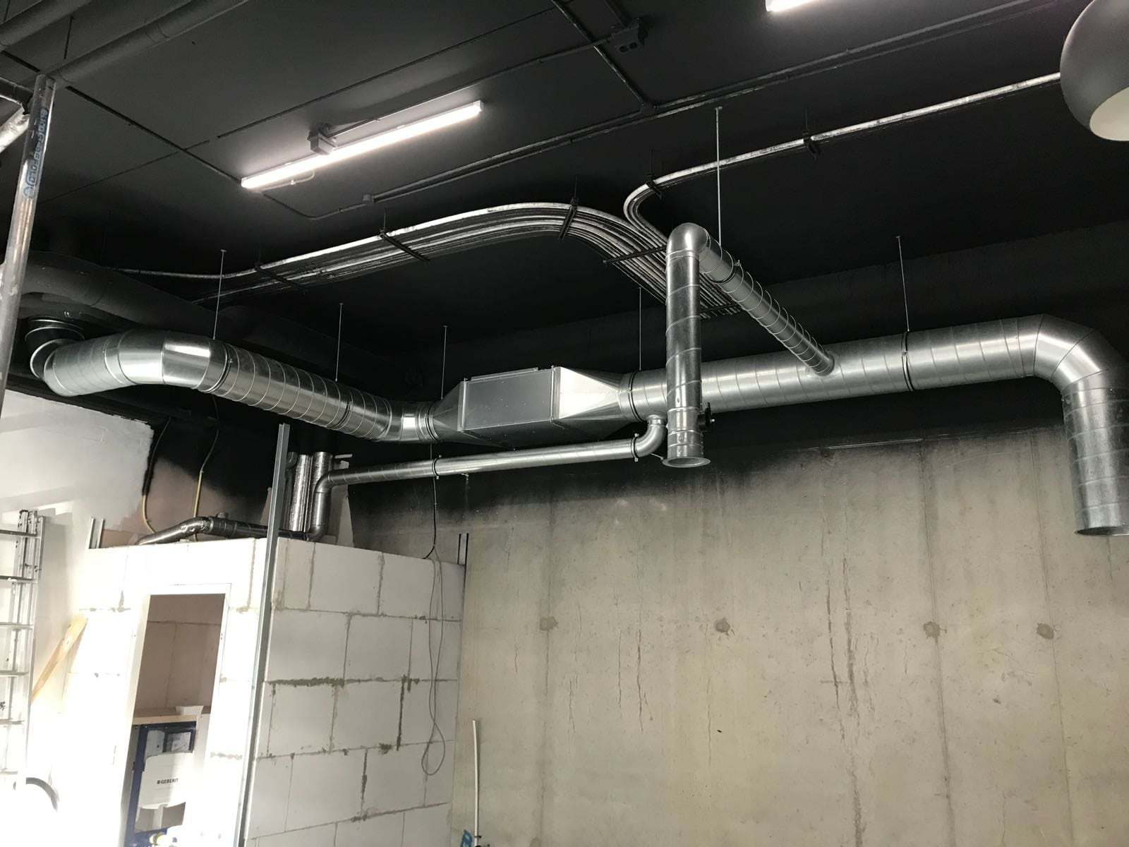 Zilveren ventilatiekanalen tegen een zwart plafond in een bedrijfsruimte